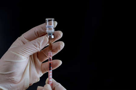 A doctor in latex gloves dials a solution of the vaccine from a vial on a black background.の写真素材