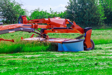 Large rotary mower mows green grass on a large field, hay for winter animals.