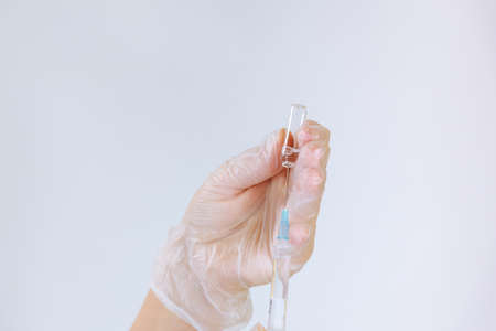 Nurse in gloves fills a syringe with a healing solution from an ampoule on a white backgroundの写真素材