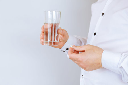 The patient holds a tablet and water in his hands, taking medication regularly.