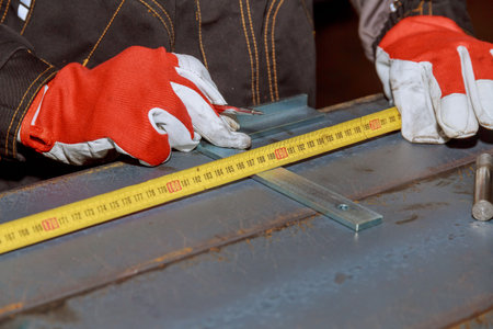 worker measures markings on a metal surface for drilling holes. The worker measures the required...