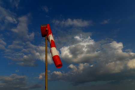 A large red white striped windsock against blue sky. Windsock wind indicator shows that there is no wind.の写真素材