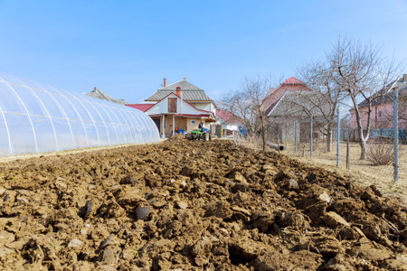 Plowed land with a small blue tractor near the greenhouse.の写真素材