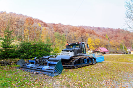 Crawler tractor stands near the forest in the autumn season. Snow collection equipment.