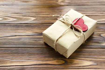 gift box wrapped in kraft paper and red wooden heart on wooden tableの写真素材
