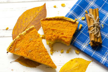 Pumpkin  pie, cinnamon sticks, autumn dry leaves on white wooden tableの写真素材
