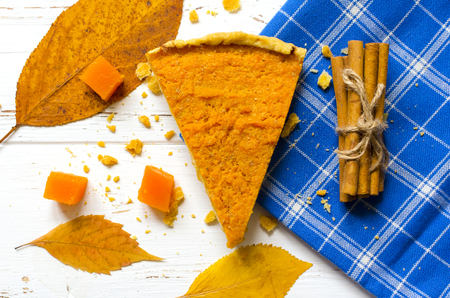 Pumpkin  pie, cinnamon sticks, autumn dry leaves on white wooden tableの写真素材