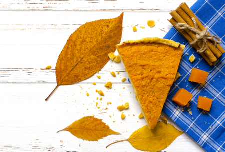Pumpkin  pie, cinnamon sticks, autumn dry leaves on white wooden tableの写真素材