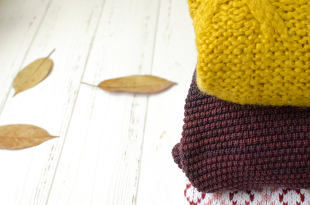 A stack of sweaters  and dry autumn leaves on white wooden backgroundの写真素材