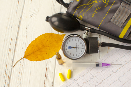 Apparatus for measuring the pressure, cardiogram, syringe, ampoule, pills and dry autumn leaf on white wooden backgroundの写真素材