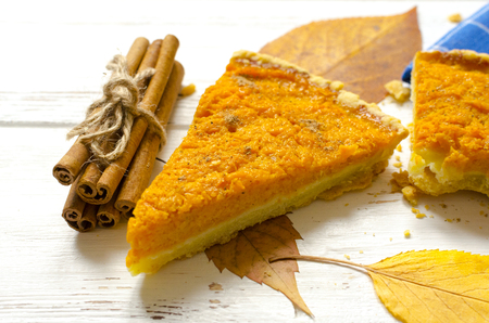 Pumpkin  pie, cinnamon sticks, autumn dry leaves on white wooden tableの写真素材