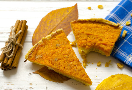 Pumpkin  pie, cinnamon sticks, autumn dry leaves on white wooden tableの写真素材