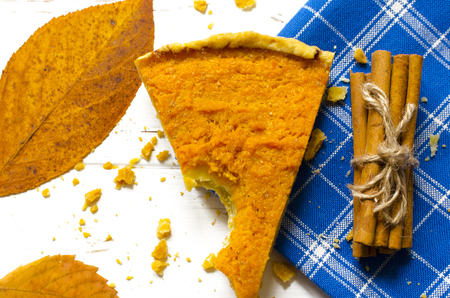 Pumpkin  pie, cinnamon sticks, autumn dry leaves on white wooden tableの写真素材