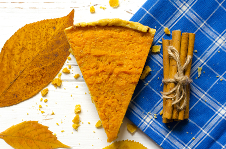 Pumpkin  pie, cinnamon sticks, autumn dry leaves on white wooden tableの写真素材