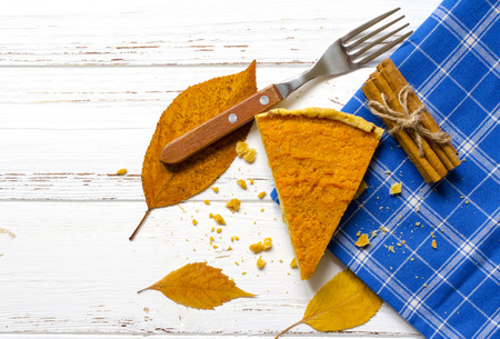 Pumpkin  pie, cinnamon sticks, autumn dry leaves on white wooden tableの写真素材