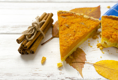 Pumpkin  pie, cinnamon sticks, autumn dry leaves on white wooden tableの写真素材