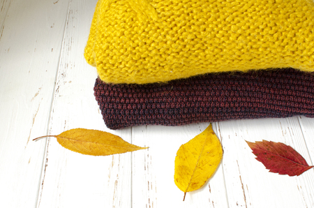 A stack of sweaters  and dry autumn leaves on white wooden backgroundの写真素材