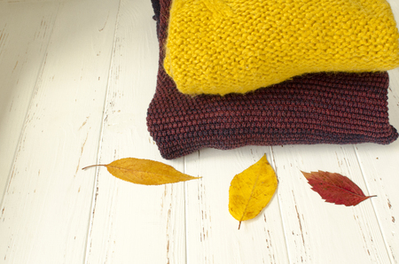 A stack of sweaters  and dry autumn leaves on white wooden backgroundの写真素材