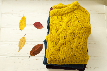 A stack of sweaters  and dry autumn leaves on white wooden backgroundの写真素材