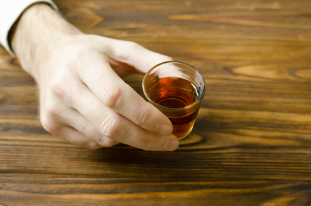 hand hold small glass with alcohol drink on wooden tableの写真素材