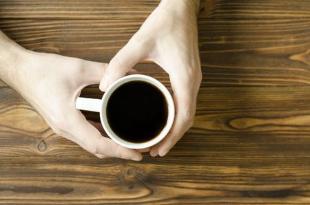 man`s hands holding a cup of coffee on wooden backgroundの写真素材