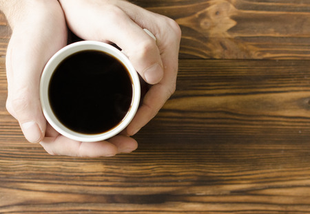 man`s hands holding a cup of coffee on wooden backgroundの写真素材