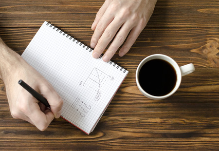  men`s hands writing in notepad and  cup  of coffee on wooden tableの写真素材