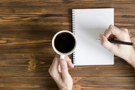  men`s hands writing in notepad and  cup  of coffee on wooden tableの写真素材