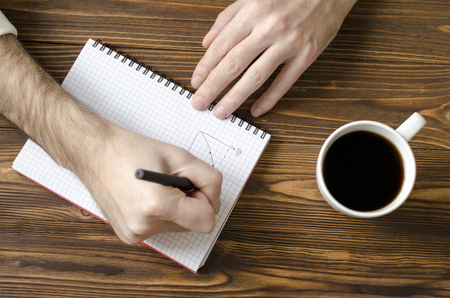  men`s hands writing in notepad and  cup  of coffee on wooden tableの写真素材