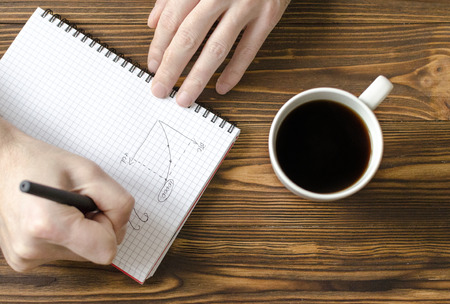  men`s hands writing in notepad and  cup  of coffee on wooden tableの写真素材
