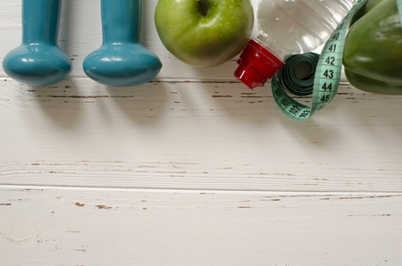 Two dumbbells, bottle of water, green apple, centimeter on white wooden background with space  for textの写真素材