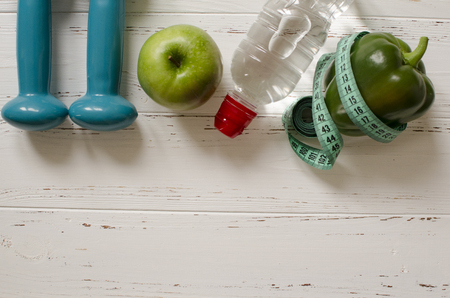 Two dumbbells, bottle of water, green apple, centimeter on white wooden background with space  for textの写真素材