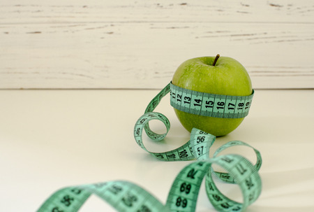 Green apple wrapped in centimeter on white wooden background with space for textの写真素材