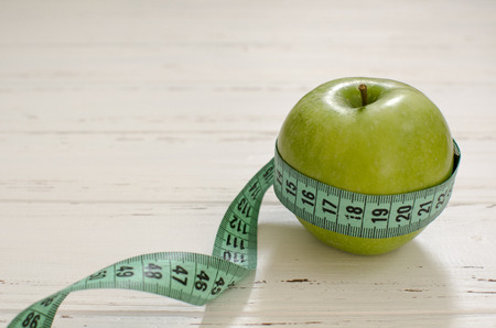 Green apple wrapped in centimeter on white wooden background with space for textの写真素材