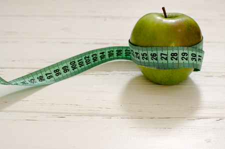 Green apple wrapped in centimeter on white wooden background with space for textの写真素材
