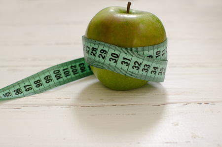 Green apple wrapped in centimeter on white wooden background with space for textの写真素材