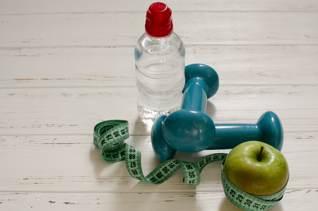Two dumbbells, bottle of water, green apple, centimeter on white wooden background with space  for textの写真素材