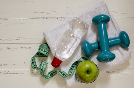 Two dumbbells, bottle of water, green apple and peppers, centimeter on white wooden background with space  for textの写真素材