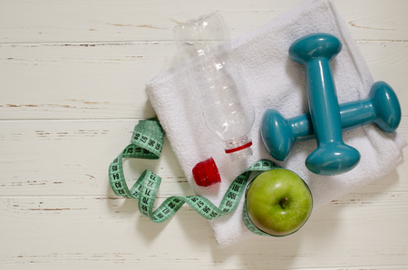 Two dumbbells, bottle of water, green apple and peppers, centimeter on white wooden background with space  for textの写真素材