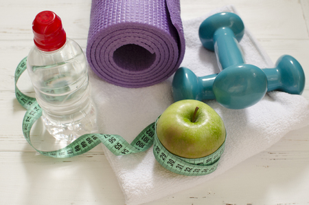Two dumbbells, bottle of water, green apple, centimeter on white wooden background with space  for textの写真素材