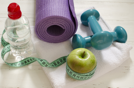Two dumbbells, bottle of water, green apple, centimeter on white wooden background with space  for textの写真素材