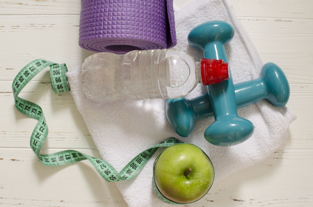 Two dumbbells, bottle of water, green apple, centimeter on white wooden background with space  for textの写真素材