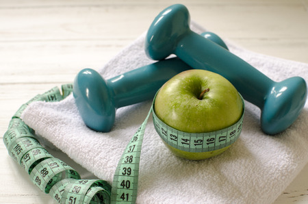 Dumbbells, green apple, towel, centimeter on white wooden background with space  for textの写真素材