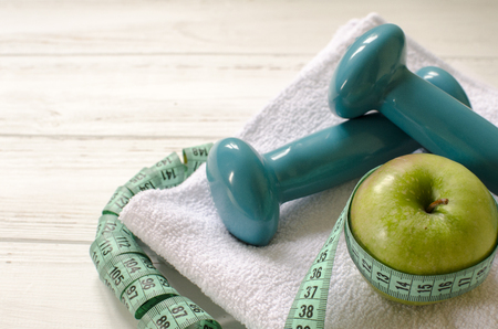 Dumbbells, green apple, towel, centimeter on white wooden background with space  for textの写真素材