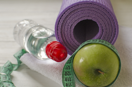 Two dumbbells, bottle of water, green apple, centimeter on white wooden background with space  for textの写真素材