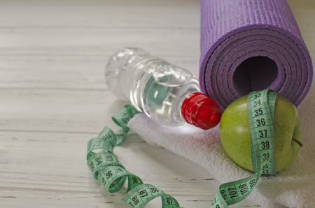 Two dumbbells, bottle of water, green apple, centimeter on white wooden background with space  for textの写真素材