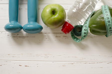 Two dumbbells, bottle of water, green apple, centimeter on white wooden background with space  for textの写真素材