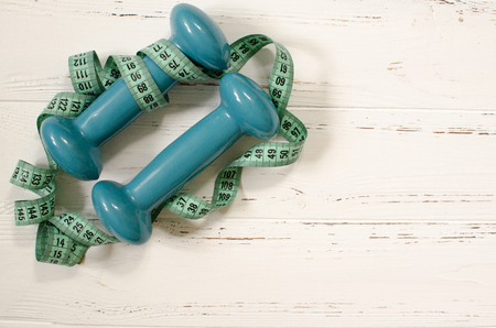 Two dumbbells, centimeter on white wooden background with space  for textの写真素材