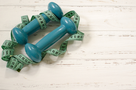 Two dumbbells, centimeter on white wooden background with space  for textの写真素材
