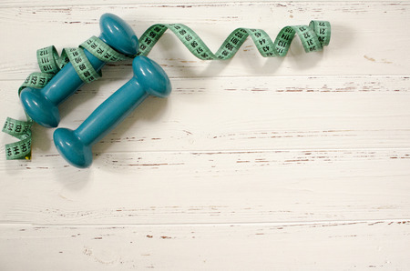 Two dumbbells, centimeter on white wooden background with space  for textの写真素材
